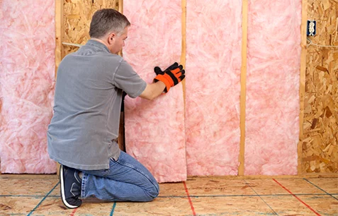 Technician removing pink fiberglass batt insulation from a wall.