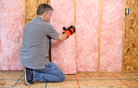 Technician removing pink fiberglass batt insulation from a wall.