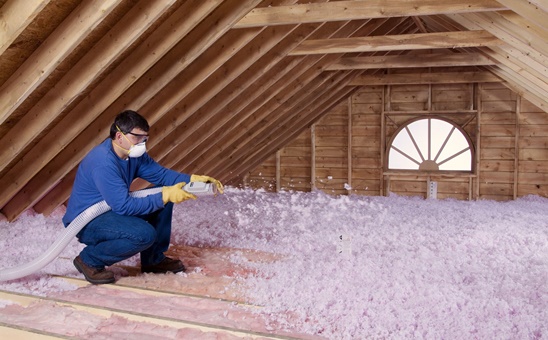 Pink blown-in insulation being installed in an unfinished attic space.